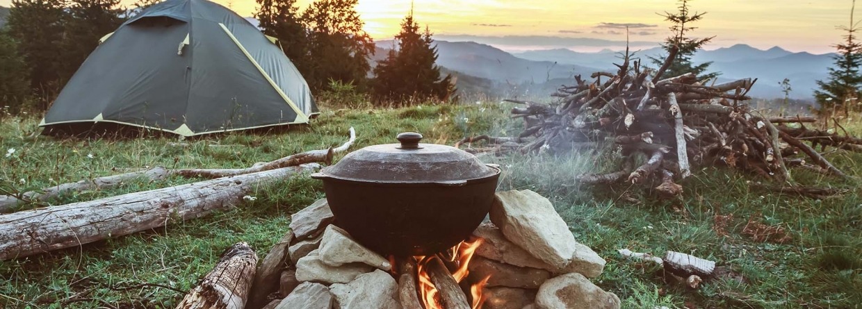 Een toerist is aan het kamperen met een tent en een kampvuur in het bos en de bergen